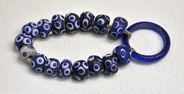 A small bracelet of round, dark blue beads covered in bright white and blue spots that are not unlike the eye of a Nazaar. There are 16 beads on the string, which terminates with a thin glass hoop, bright blue in color.
