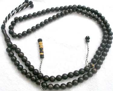 A 104 bead masbaha with perfectly spherical black marble beads and three counter strings. One of the strings has 10 flat, round counters. Three black and white striped strings come out of the Imam bead, one of which also has ten counters.