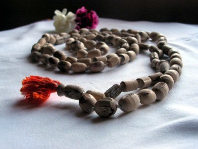 Closeup of a tulsi bead mala in soft white lighting. The beads are rough hewn, rounded cylinders in a soft, pale wood, with a matte texture. The final meru bead has an orange-red tassle at the end