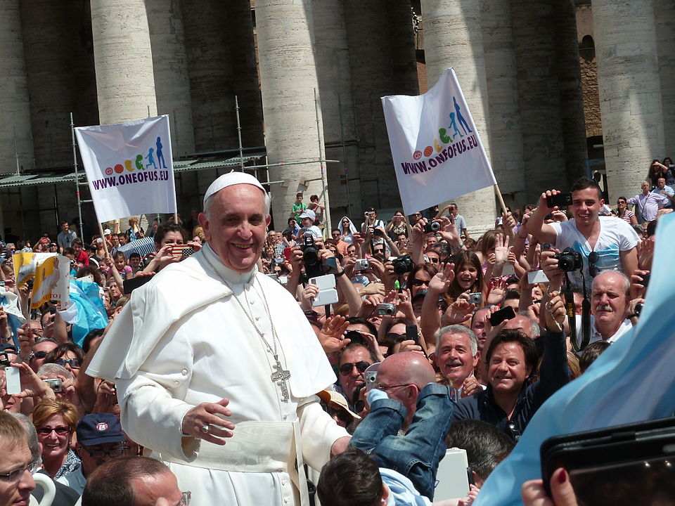 Picture of Pope Francis smiling, surrounded by a crowd of happy looking people, some holding rainbow signs that say "one of us".